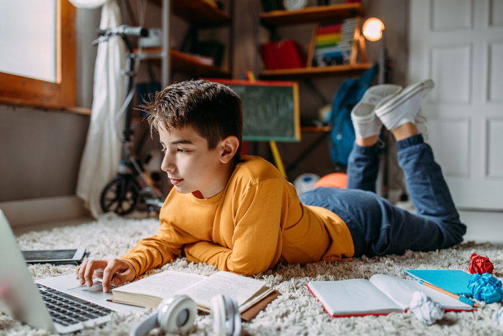 Teenage boy doing homework Boy lying on the floor using computer