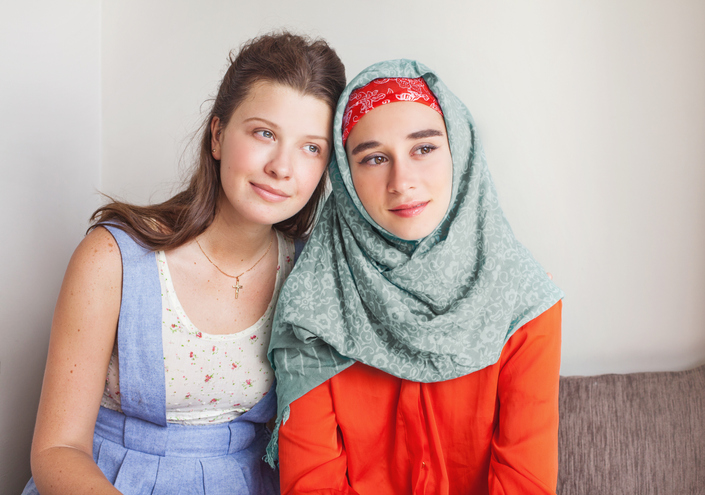 Two girls sat together, one is wearing a head covering.