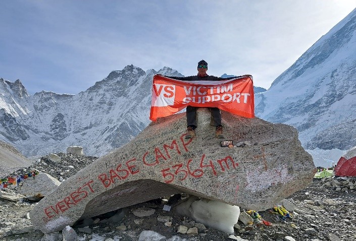 Man holding a Victim Support banner sat on a boulder