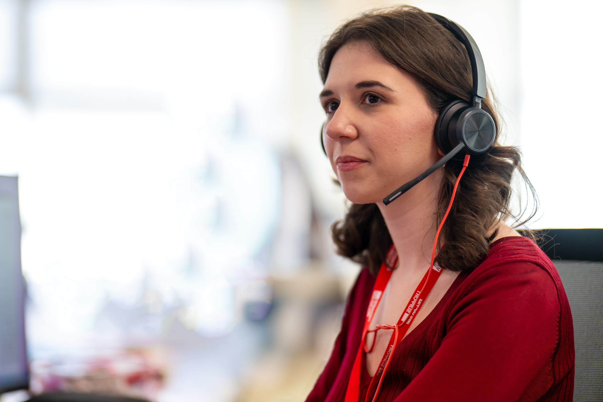 Photo of a female Victim Support staff member with a headset and red lanyard, seated at a desk in front of a computer.