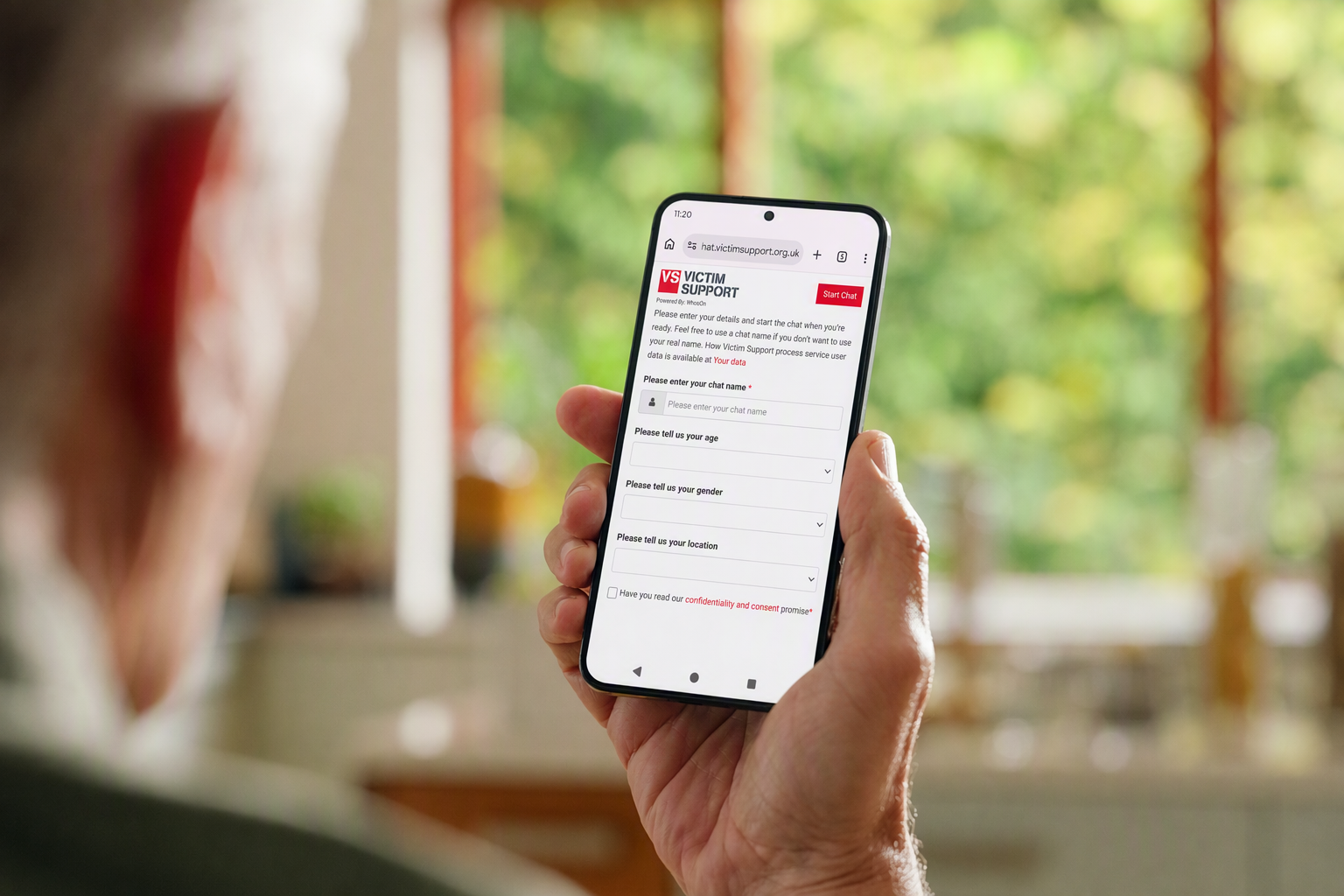 Photo of an older gentleman holding a smartphone showing the Victim Support live chat page.